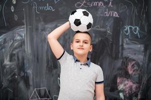 menino feliz segurando uma bola de futebol na cabeça foto