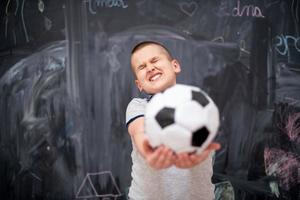 menino feliz segurando uma bola de futebol na frente do quadro-negro foto