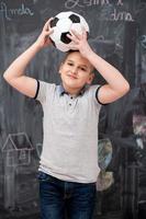 menino feliz segurando uma bola de futebol na cabeça foto
