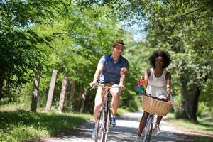 jovem casal multiétnico dando um passeio de bicicleta na natureza foto