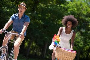 jovem casal multiétnico dando um passeio de bicicleta na natureza foto