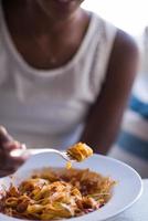 uma jovem afro-americana comendo macarrão foto