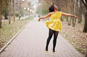 elegante mulher afro-americana no vestido amarelo posou contra o parque outono e pulando. foto