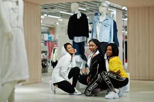 três mulheres afro-americanas em agasalhos fazendo compras no shopping de roupas esportivas contra manequim. tema da loja de esportes. foto