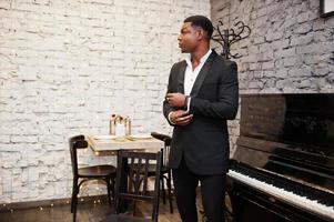 forte e poderoso homem afro-americano de terno preto em pé contra o piano. foto
