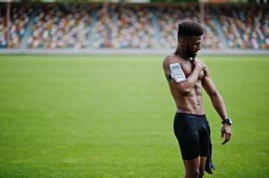 atleta masculino americano africano homem sexy torso nu esporte com capa de braço de esportes em execução para telefone celular, posou na grama verde do estádio de futebol. foto