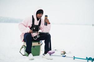 pescador americano africano com vara de pescar e garrafa térmica. pesca de inverno. foto