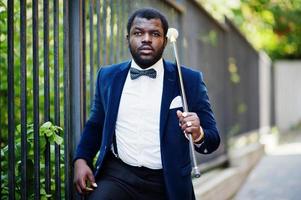 homem afro-americano elegante bonito com roupa formal e gravata borboleta com bengala. foto