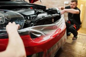 trabalhador de serviço de carro colocou filme anti cascalho em um corpo de carro vermelho na oficina de detalhamento de veículos. proteção do carro com películas especiais. foto