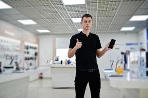 vendedor homem consultor profissional de celular na loja de tecnologia ou loja segure o novo smartphone à mão e mostre o polegar para cima. foto