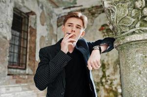 jovem macho vestindo jaqueta elegante blac fumando cigarro nas ruas. foto