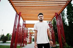 homem de barba indiana elegante na camiseta rosa. modelo da índia posou sob o arco vermelho no parque da cidade. foto