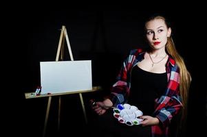 pintor de artista de mulher bonita com pincéis e tela a óleo posando em estúdio isolado em preto. foto