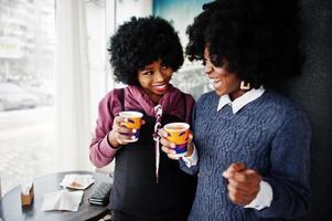 duas mulheres afro-americanas de cabelo encaracolado usam suéteres com xícaras de chá posadas no café interior. foto