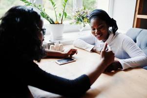 duas garotas afro-americanas sentadas na mesa no café e procurando algo no celular. foto