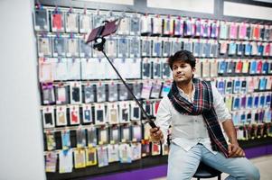comprador de cliente homem indiano na loja de celular fazendo selfie por smartphone na vara monopé. conceito de povos e tecnologias do sul da Ásia. loja de celulares. foto