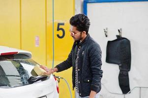 homem do sul da Ásia ou homem indiano lavando seu transporte branco na lavagem de carros. foto