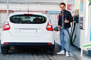 homem do sul da Ásia ou homem indiano reabastecendo seu carro branco no posto de gasolina. foto