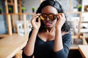 feche o rosto da garota afro-americana em óculos de sol posou no café moderno. foto