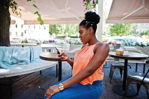 garota afro-americana sentada na mesa de caffe com telefone celular. foto