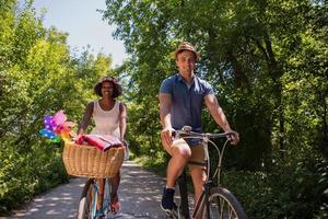 jovem casal multiétnico dando um passeio de bicicleta na natureza foto