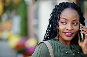 elegantes mulheres afro-americanas na camisola verde e saia preta posaram café ao ar livre com uma xícara de café e falar no celular. foto