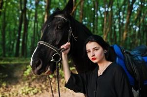 garota mística veste de preto com cavalo em madeira. foto