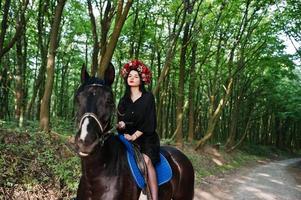 garota mística em grinalda veste de preto a cavalo em madeira. foto