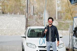 homem do sul da Ásia ou homem indiano lavando seu transporte branco na lavagem de carros. foto