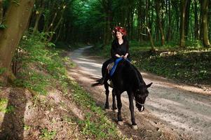 garota mística em grinalda veste de preto a cavalo em madeira. foto