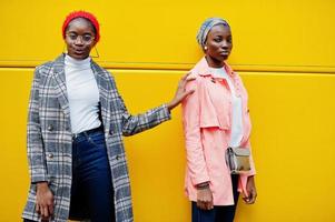 duas jovens mulheres muçulmanas africanas elegantes, atraentes, altas e magras em hijab ou lenço de cabeça de turbante e casaco posaram contra ônibus amarelo. foto