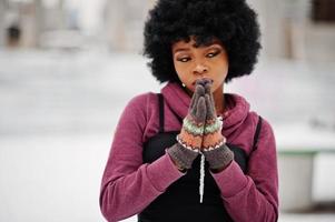 mulher afro-americana de cabelo encaracolado com luvas, mãos juntas como rezar, posou em dia de inverno. foto