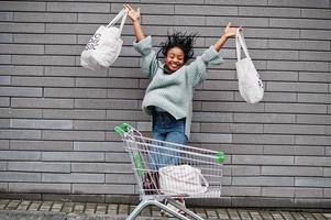 não mais plástico. mulher africana com carrinho de compras e sacolas ecológicas saltam no mercado ao ar livre. foto