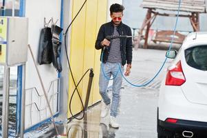 homem do sul da Ásia ou homem indiano lavando seu transporte branco na lavagem de carros. foto