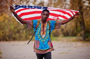 homem africano na camisa tradicional da África no parque outono com bandeira dos eua. foto