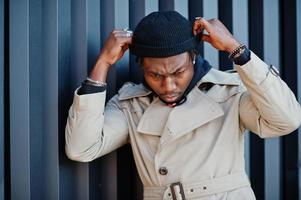 homem afro-americano bonito posando lá fora no chapéu preto e casaco bege. foto