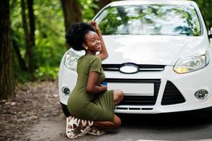 mulher afro-americana posou contra carro branco na estrada florestal. foto