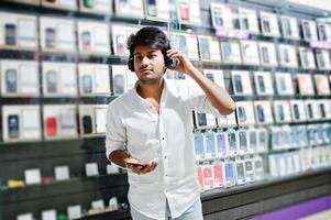 comprador de cliente homem indiano na loja de telefones móveis ouve música de fones de ouvido sem fio conectar ao seu smartphone. conceito de povos e tecnologias do sul da Ásia. loja de celulares. foto