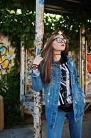 garota elegante hipster casual em jeans e óculos contra a grande parede de graffiti. foto