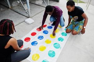 grupo de três amigos afro-americanos jogam o jogo twister ao ar livre. foto