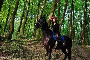garota mística em grinalda veste de preto a cavalo em madeira. foto