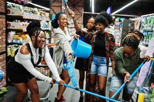 grupo de cinco mulheres africanas com esfregão, escova de vaso sanitário e balde se divertindo no departamento de itens de limpeza doméstica no supermercado. foto