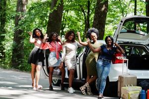 grupo de cinco meninas viajantes afro-americanas felizes posaram contra o porta-malas aberto do carro. foto