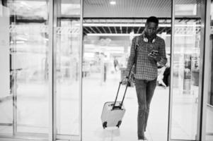 homem afro-americano de camisa quadriculada, com mala e mochila. viajante negro no duty free. foto