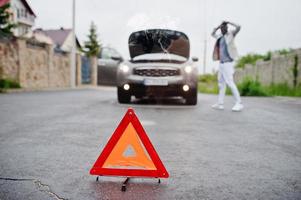 triângulo de aviso vermelho de emergência no carro suv quebrado do sinal de estrada do homem africano. foto