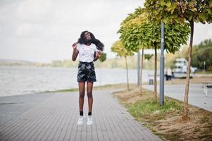 modelo magro de pele escura afro-americana posou em um short de couro preto e camiseta branca. ela pulando no ar. foto