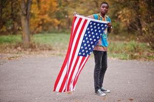 homem africano na camisa tradicional da África no parque outono com bandeira dos eua. foto