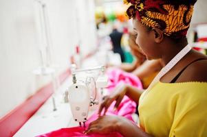 mulher de duas costureiras africanas costura roupas na máquina de costura no escritório do alfaiate. meninas costureiras negras. foto