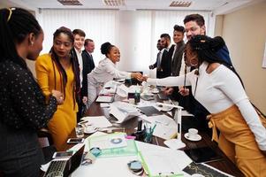 bom negócio. equipe de negócios multirracial abordando a reunião em torno da mesa da diretoria e apertando as mãos um do outro. foto