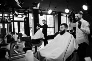 homem barbudo bonito na barbearia, barbeiro no trabalho, usando secador de cabelo. foto